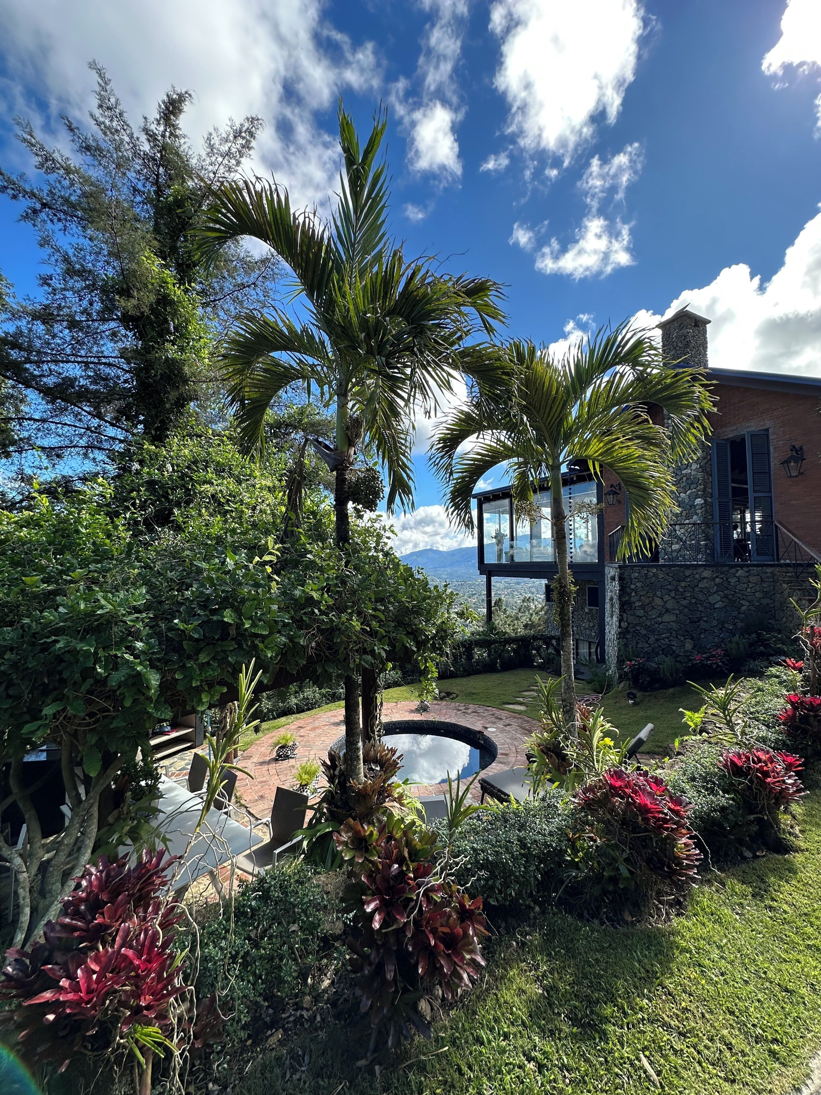 A landscaped garden with a pool, palm trees, and a stone building with a glass viewing area.
