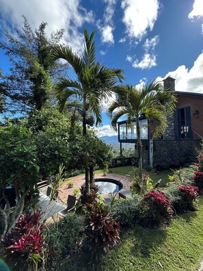 Ein angelegter Garten mit Pool, Palmen und einem Steinhaus mit einer Glasgalerie.