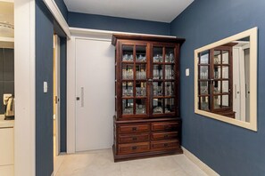 Una habitación con una pared azul oscuro, un mueble de madera con puertas de cristal, una puerta blanca y un espejo en la pared.