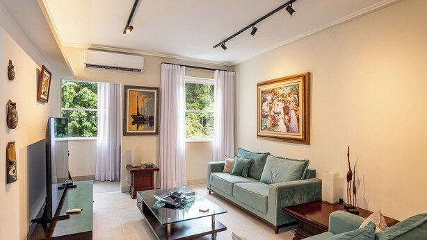 A living room with a sofa, a coffee table, a TV, and a painting on the wall. - Leme 300 m praia 2 quartos conforto (Rio de Janeiro)