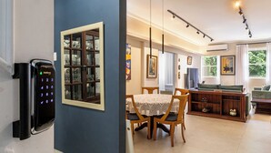A dining area with a table and chairs, a bookshelf, and a wall-mounted security device. - Leme 300 m praia 2 quartos conforto (Rio de Janeiro)