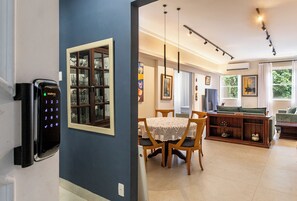 Un comedor con mesa y sillas, una estantería y un dispositivo de seguridad fijado a la pared.