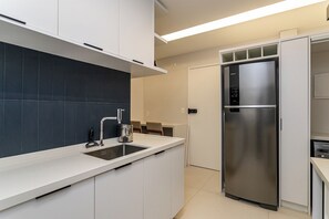 Una cocina moderna con armarios blancos, un refrigerador de acero inoxidable y un salpicadero de azulejos oscuros.