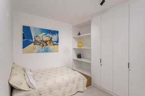 Un dormitorio con cama, un cuadro, un armario blanco y una estantería con objetos decorativos.