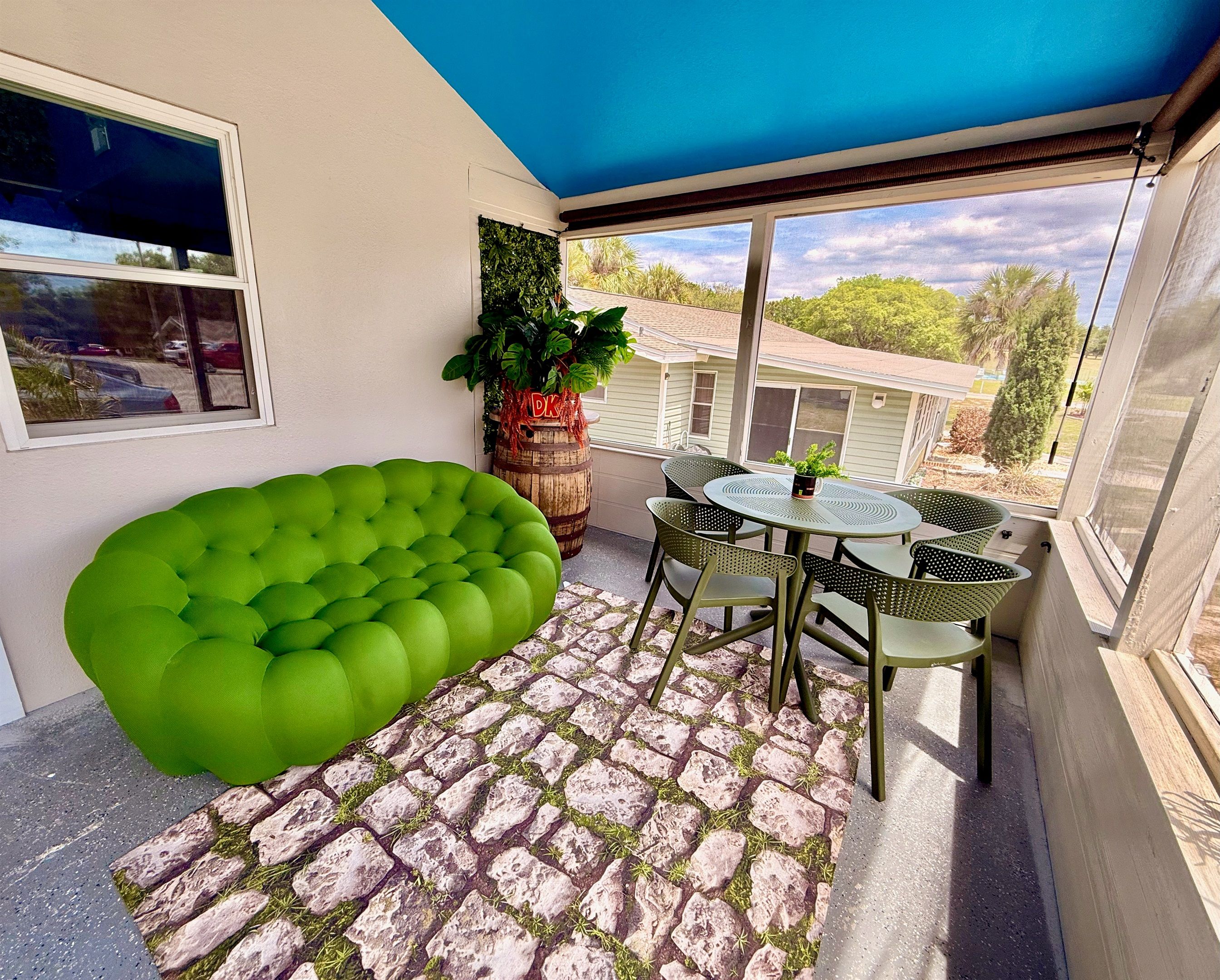 Een balkon met een groene, beklede zithoek, een ronde tafel met stoelen en een potplant.
