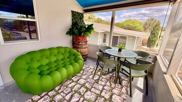 Een balkon met een groene, beklede zithoek, een ronde tafel met stoelen en een potplant.