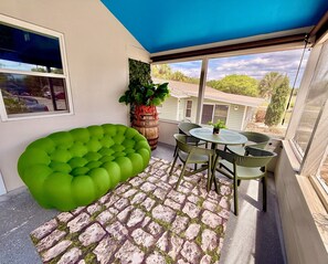 Un balcon doté d’un espace salon avec des coussins verts, d’une table ronde avec des chaises et d’une plante en pot.