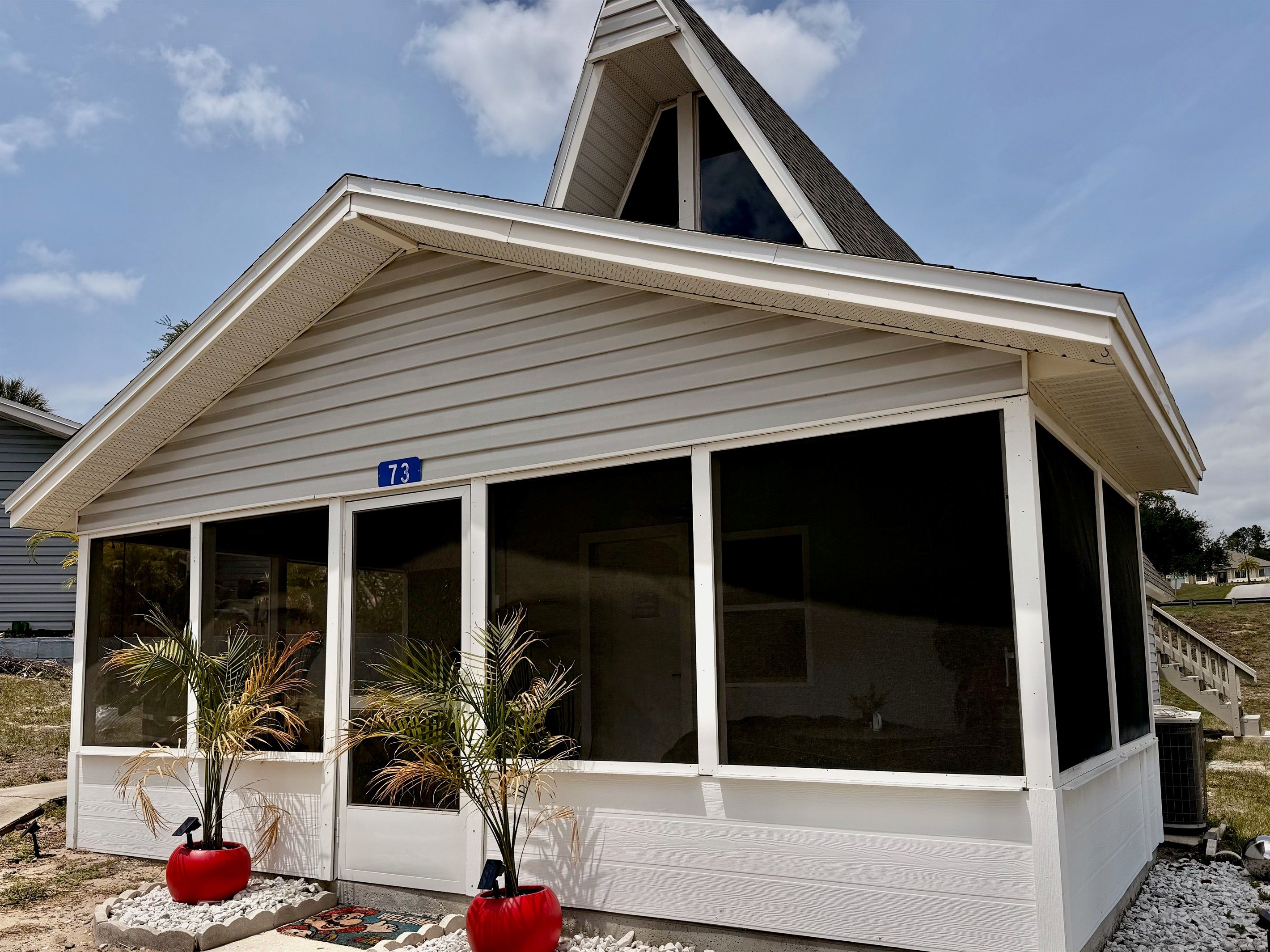 A house with a covered porch, a number sign '73', and two potted plants.