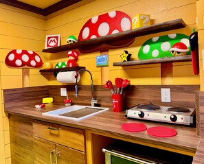 Een keuken met houten kastjes, een spoelbak, een fornuis en planken met paddenstoelvormige decoraties.