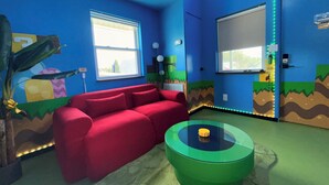 Een kamer met een rode bank, een groene tafel en blauwe muren met cartooneske muurschilderingen.