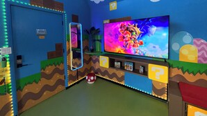 Een kamer met een grote televisie, een deur en een plank met spullen.