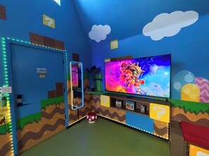 A room with a large TV, a door, and a shelf with items. - Mario's Mini Mansion: Themed Family Fun in Clermont, Florida! Locals Welcome (Clermont)