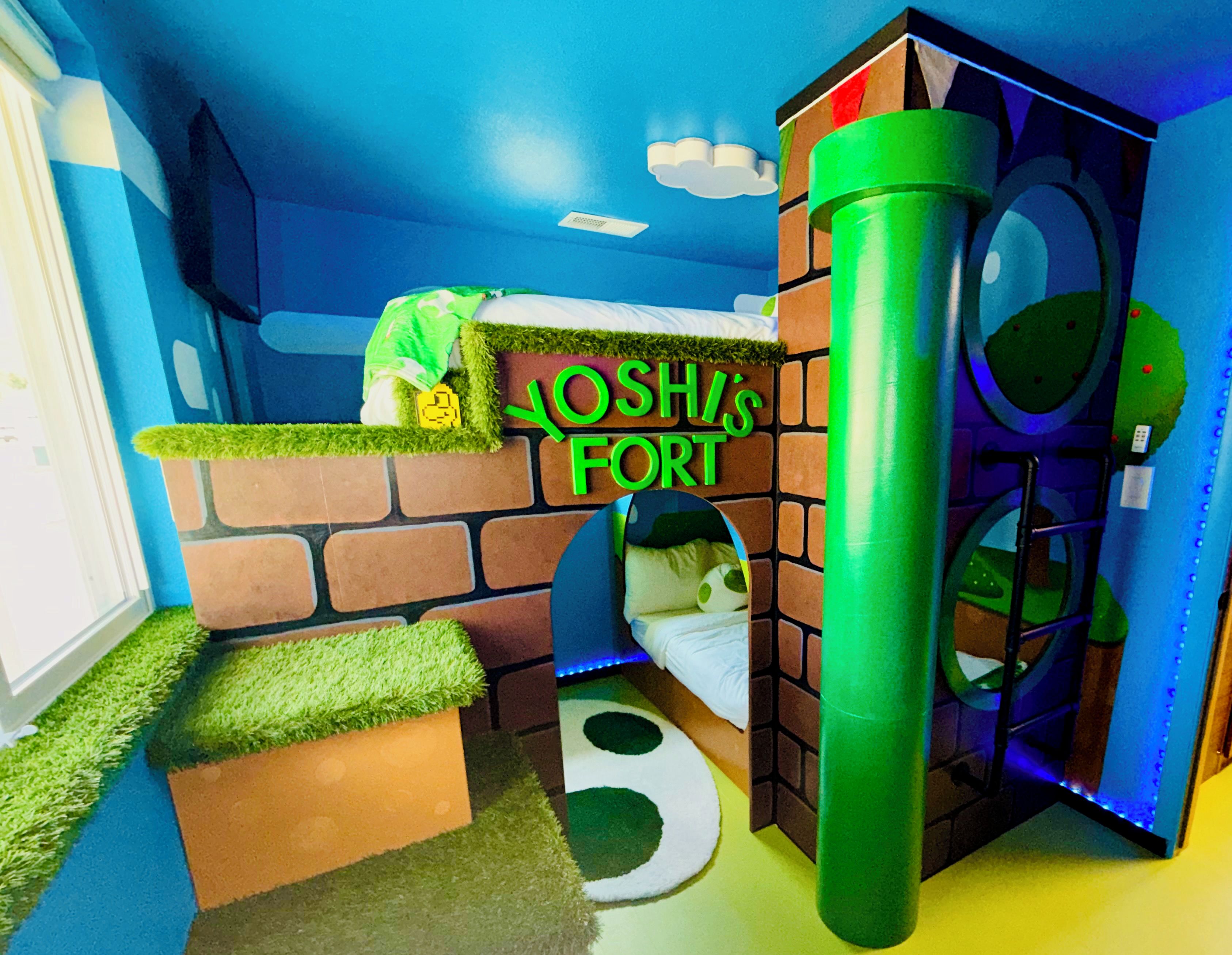 Een kinderspeelruimte met een bakstenen muur, een groene speelconstructie en een bord waarop staat 'YOSHIS FORT'.