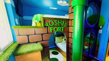 Een kinderspeelruimte met een bakstenen muur, een groene speelconstructie en een bord waarop staat 'YOSHIS FORT'.