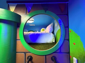 A circular window with a bed inside, a wall with a green door, and a blue wall with a sign. - Mario's Mini Mansion: Themed Family Fun in Clermont, Florida! Locals Welcome (Clermont)