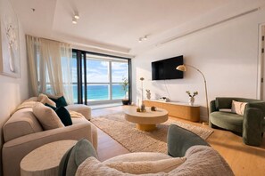 Ein modernes Wohnzimmer mit Sofa, Sessel, Couchtisch und einem an der Wand befestigten Fernseher.