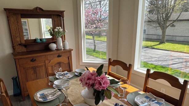 A dining table set with plates, glasses, and a vase of flowers, with a view of a tree outside. - Spacious downtown oasis, free parking & laundry (Bellingham)