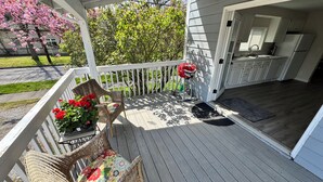 A covered porch with wicker chairs and a table, a small garden with pink flowers, and a view of a house with a kitchen. - Spacious downtown oasis, free parking & laundry (Bellingham)