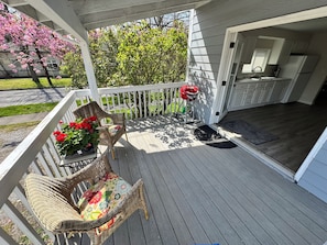 A covered porch with wicker chairs and a table, a small garden with pink flowers, and a view of a house with a kitchen. - Spacious downtown oasis, free parking & laundry (Bellingham)