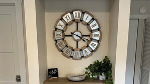 A wall-mounted clock with Roman numerals, a small shelf with a bowl and a sign, a potted plant, and a trash can in a hallway. - Spacious downtown oasis, free parking & laundry (Bellingham)