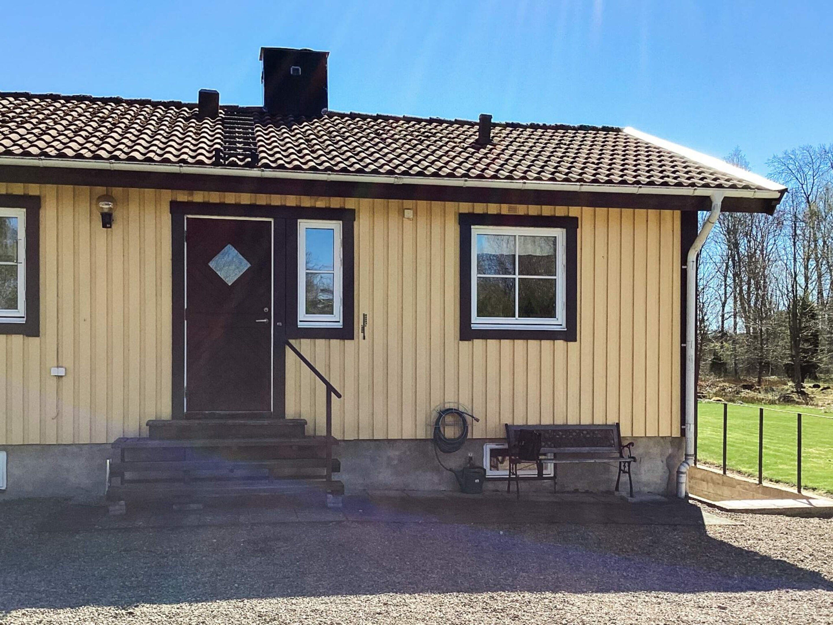 Ein eingeschossiges Gebäude mit einer braunen Tür, zwei Fenstern und einer kleinen Veranda mit Stufen zum Eingang.