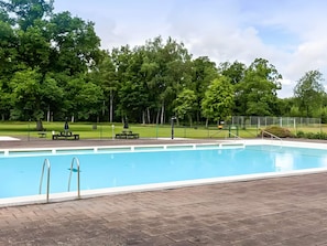 A swimming pool with a paved deck, surrounded by trees and a grassy area. - 6 Person Holiday Home in Ljungbyhed (Ljungbyhed)