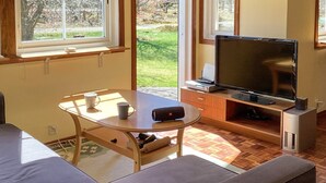 A living room with a sofa, a table with two mugs, a television on a stand, and a window with a view of greenery. - 6 Person Holiday Home in Ljungbyhed (Ljungbyhed)