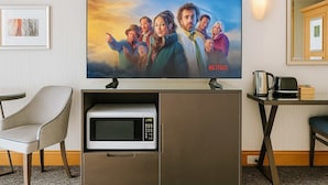 A hotel room with a flat-screen TV mounted on a cabinet, a microwave, a coffee maker, and a chair. - Stunning Ocean View Studio Pool, Spa & Wi-Fi (Surfers Paradise)