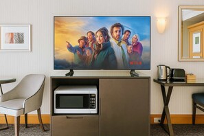 Ein Hotelzimmer mit Flachbildfernseher an einer Schrankwand, einer Mikrowelle, einer Kaffeemaschine und einem Sessel.
