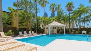 A swimming pool with lounge chairs and a gazebo, surrounded by palm trees and buildings. - Stunning Ocean View Studio Pool, Spa & Wi-Fi (Surfers Paradise)