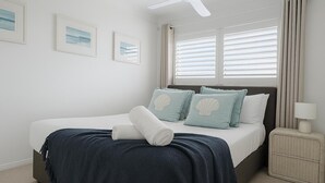 A bedroom with a bed, pillows, a bedside lamp, and a window with blinds. - Magic Nobby Beach 3BR Apt (Miami)