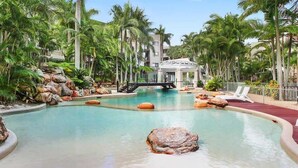 A pool with rocks, palm trees, and a bridge. - Magic Nobby Beach 3BR Apt (Miami)