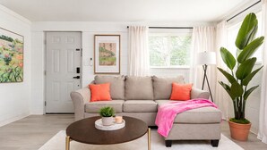 A living room with a sectional sofa, a coffee table, a potted plant, and a door. - NEW Owner Special King Bed Colorful Quay Themed Duplex Workspace Fuquay-Varina (Fuquay-Varina)