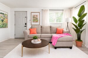 A living room with a sectional sofa, a coffee table, a potted plant, and a door.