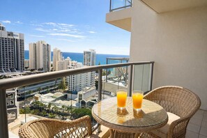 A balcony with wicker chairs and a table, two glasses of orange juice, and a cityscape view. - L17 Small Studio Suite 2 Beds Pool Spa (Surfers Paradise)