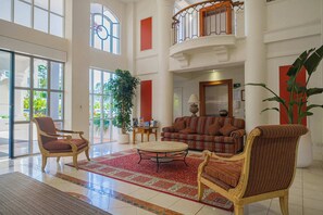 A spacious lobby with a high ceiling, large windows, a central round table, and a seating area with sofas and armchairs. - 1BR Tropical Escape w/ Pools (Surfers Paradise)