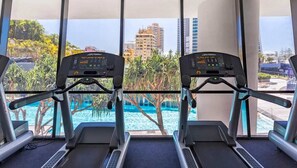 A treadmill area with a view of a pool and buildings. - Ocean View Designer Apt SPA Wi-Fi (Surfers Paradise)