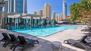A rooftop pool with lounge chairs, a glass building, and high-rise buildings in the background. - Ocean View Designer Apt SPA Wi-Fi (Surfers Paradise)