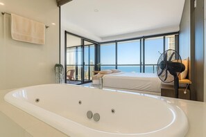 A modern bedroom with a large bathtub, a bed, and a view of the city skyline. - Ocean View Designer Apt SPA Wi-Fi (Surfers Paradise)