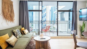 Una sala de estar moderna con un sofá verde, una mesa de centro redonda y un balcón con vistas a edificios altos.