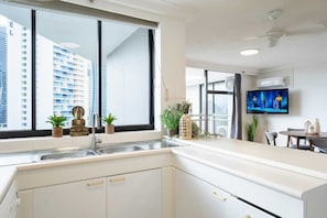 A modern kitchen with a large window, a flat-screen TV, and a dining area with a table and chairs. - High Level 1BR Apartment 1 MIN to Beach (Surfers Paradise)