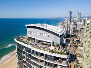 A modern hotel with a rooftop terrace, named 'RHAPSOY,' overlooking a beach and city skyline. - Level 11 Ocean view Escape (Surfers Paradise)