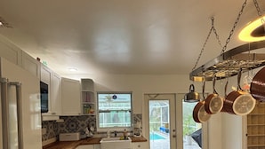 Uma cozinha moderna com armários brancos, bancada de madeira e um suporte para panelas pendurado.