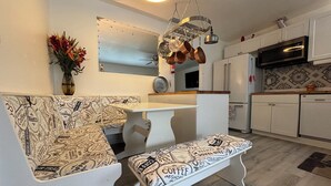 Uma cozinha moderna com armários brancos, um suporte para panelas suspenso, um banco branco com estofamento temático de café e um espelho decorativo sobre o balcão.