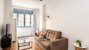 A living room with a sofa, a coffee table, a TV, a ceiling fan, and a window with curtains. - Copacabana 2 quartos e vista mar (Rio de Janeiro)