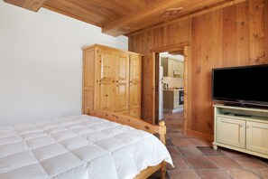 Un dormitorio con una cama de madera, un televisor sobre un mueble y paredes de madera.
