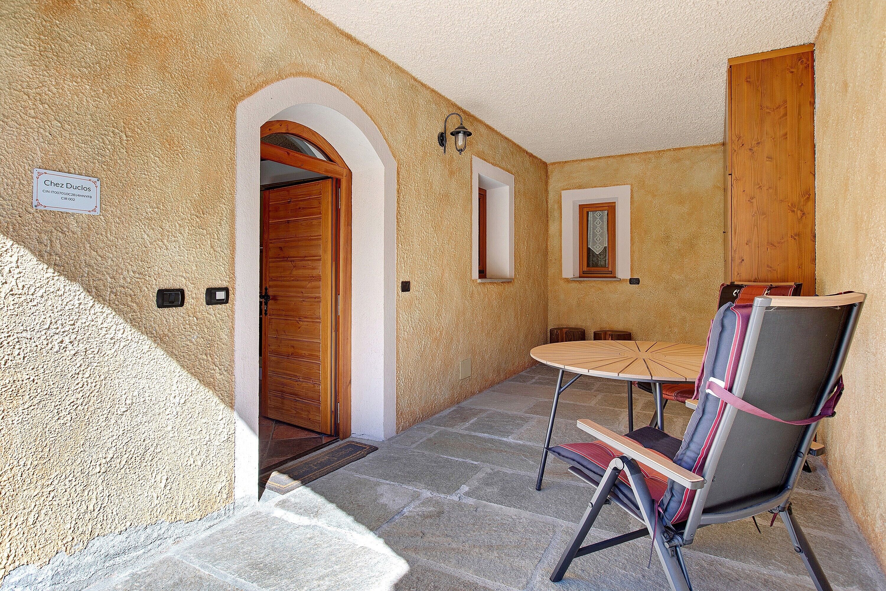 A room with a stone floor, a wooden door, a table with chairs, and a sign reading 'Chez Duclos.'