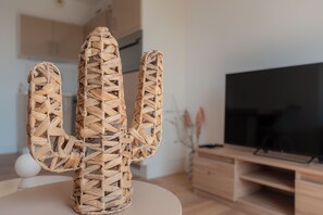 A woven cactus sculpture on a table in a modern living room with a flat-screen TV and wooden furniture. - Elegant new T2 with sea view, pool and gym in a refined setting. (Mandelieu-la-Napoule)