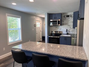A kitchen with granite countertops, dark cabinets, stainless steel appliances, and a window with blinds. - Bangor Waterfront Stay Steps to Concert Venue (Bangor)