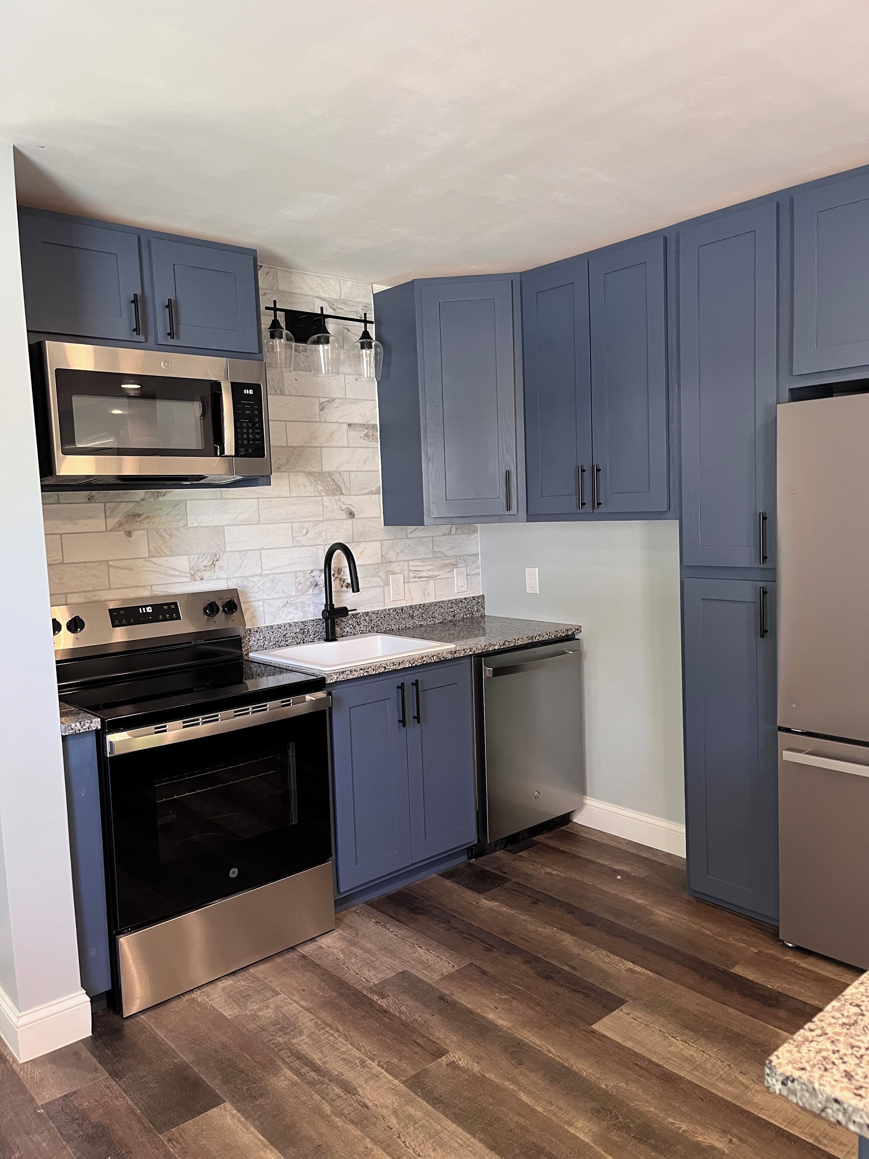 Una cocina moderna con electrodomésticos de acero inoxidable, armarios grises, salpicadero de mármol y suelo de madera.